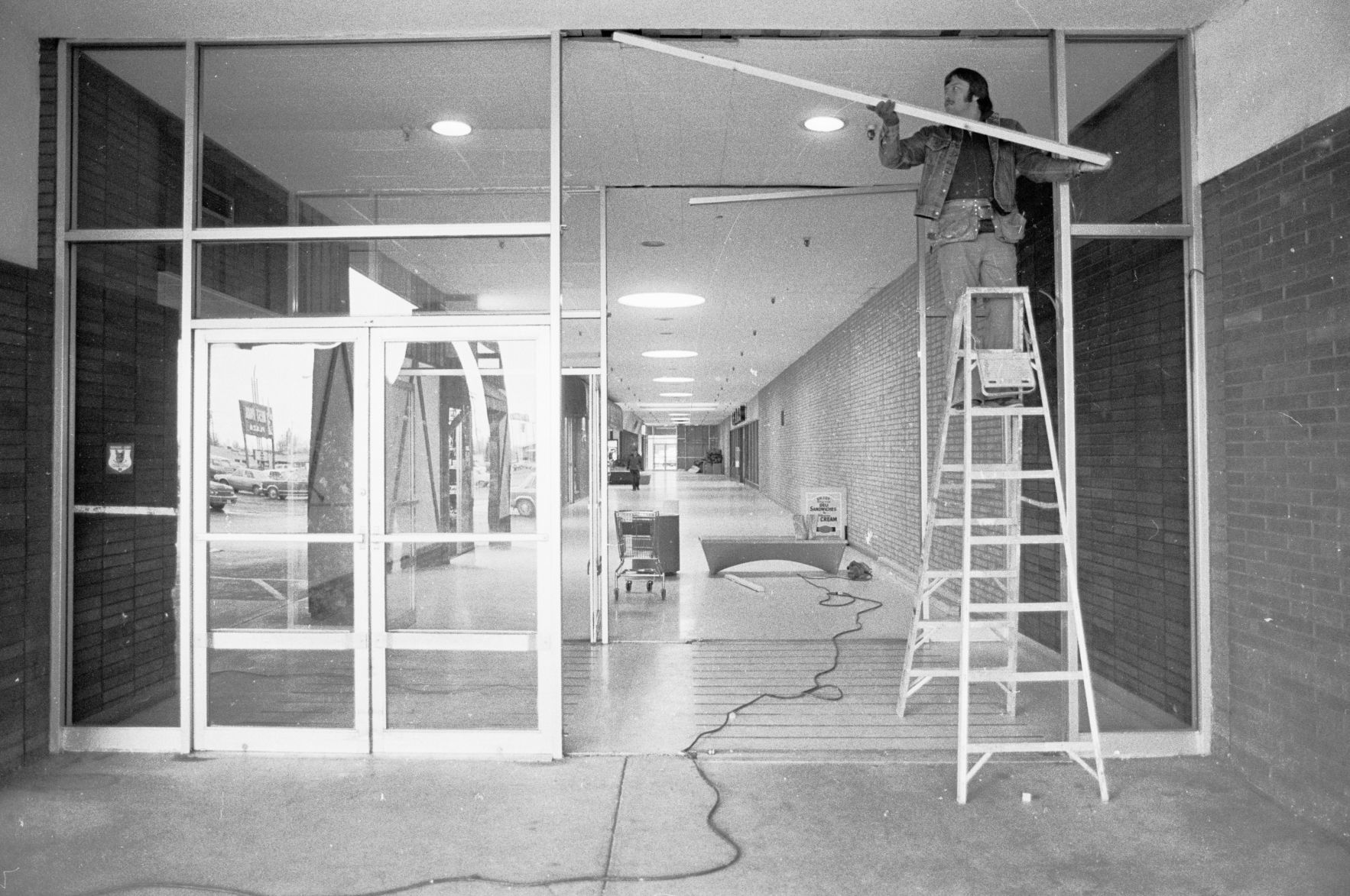 Worker repairs damage done by car crashing into West Park Plaza entrance, 1980